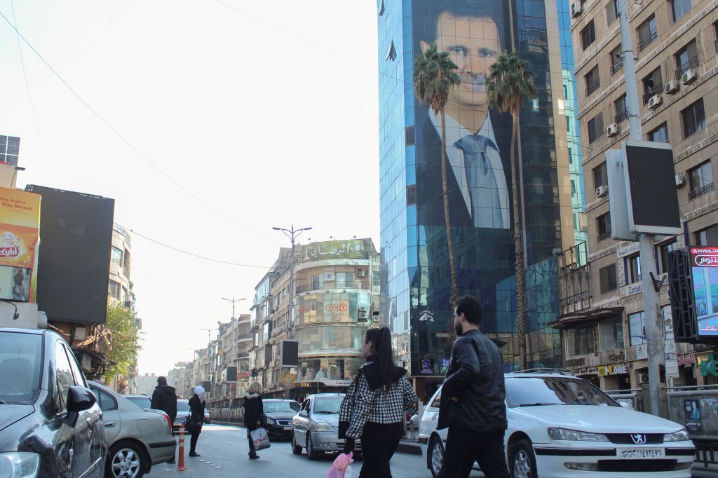 Pessoas caminham perto de pôster com a imagem do presidente da Síria, Bashar al-Assad, em Damasco.